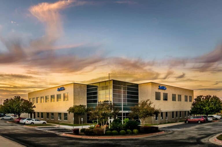 An office building at sunset with cars parked in front of it.