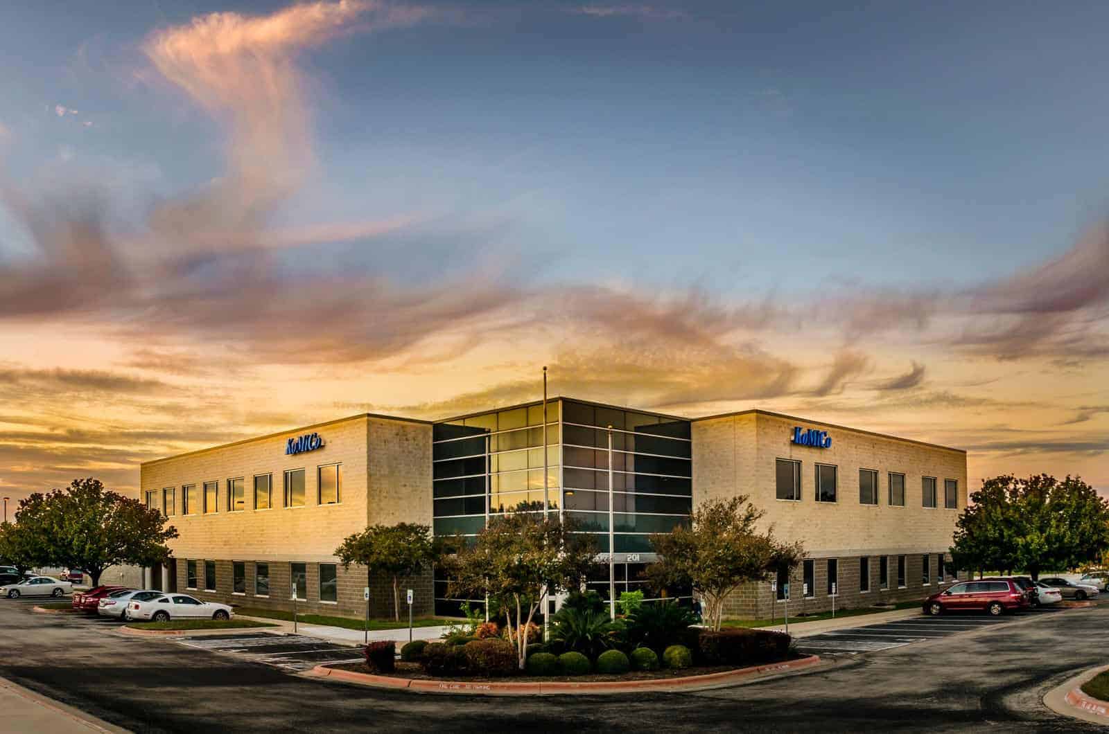 An office building at sunset with cars parked in front of it.