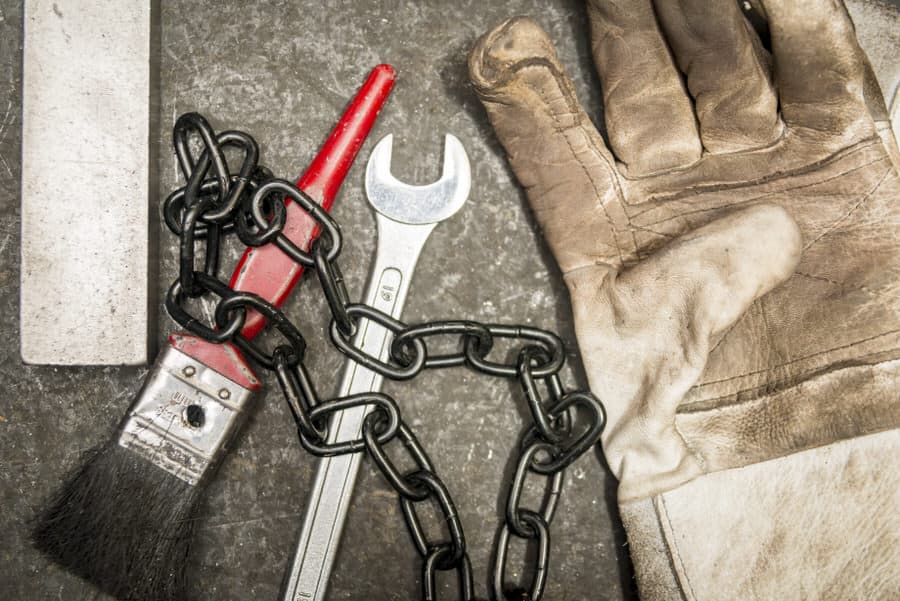 A pair of gloves, a wrench, and a chain on a concrete surface.