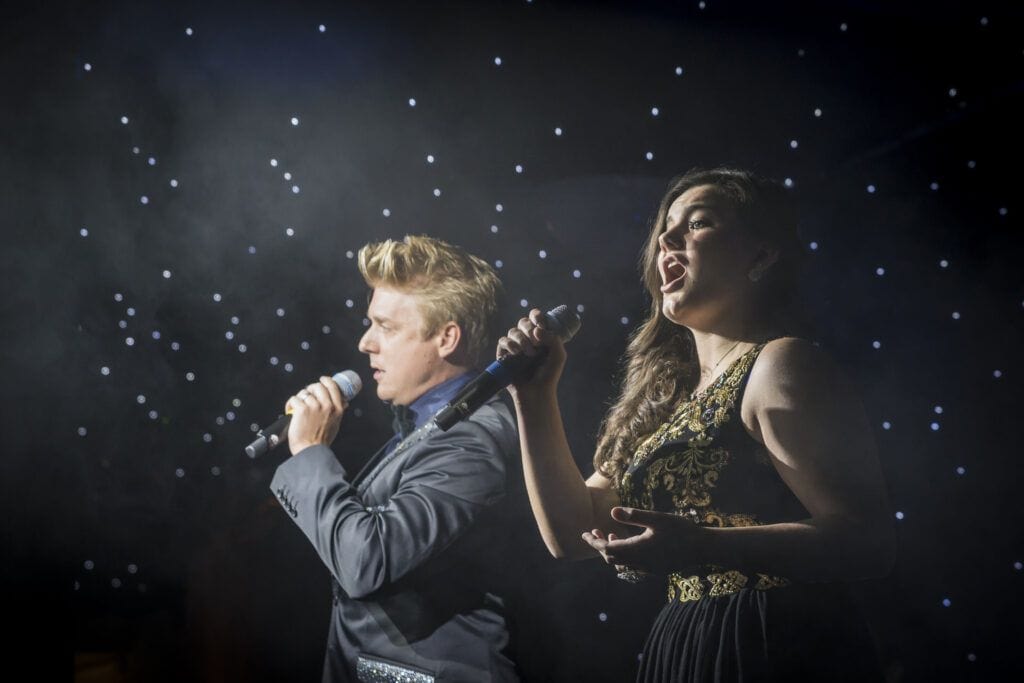 A man and a woman singing into a microphone.