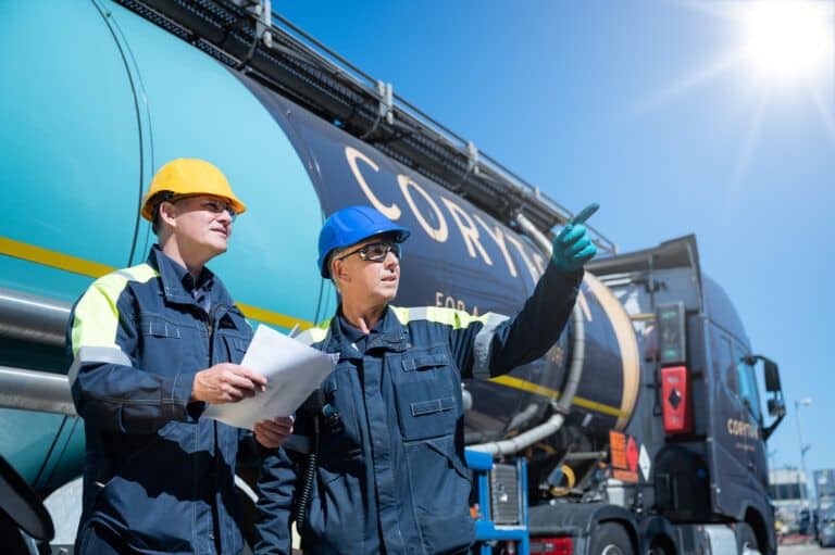 Two men in hard hats standing next to a large truck.