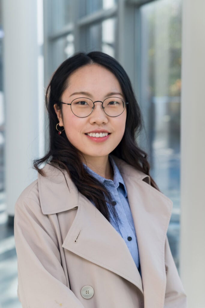 A young woman wearing glasses and a trench coat.
