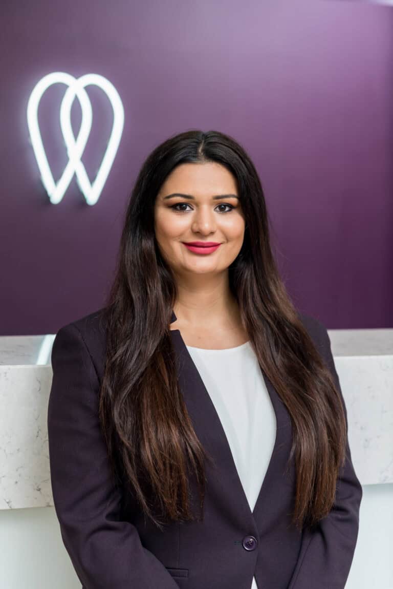 A woman in a business suit standing in front of a purple wall.