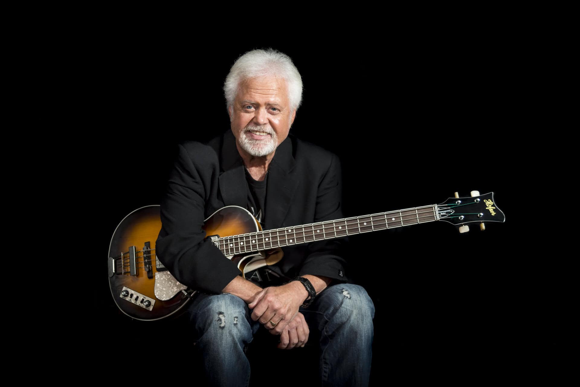 A man sitting on a black background with a guitar.