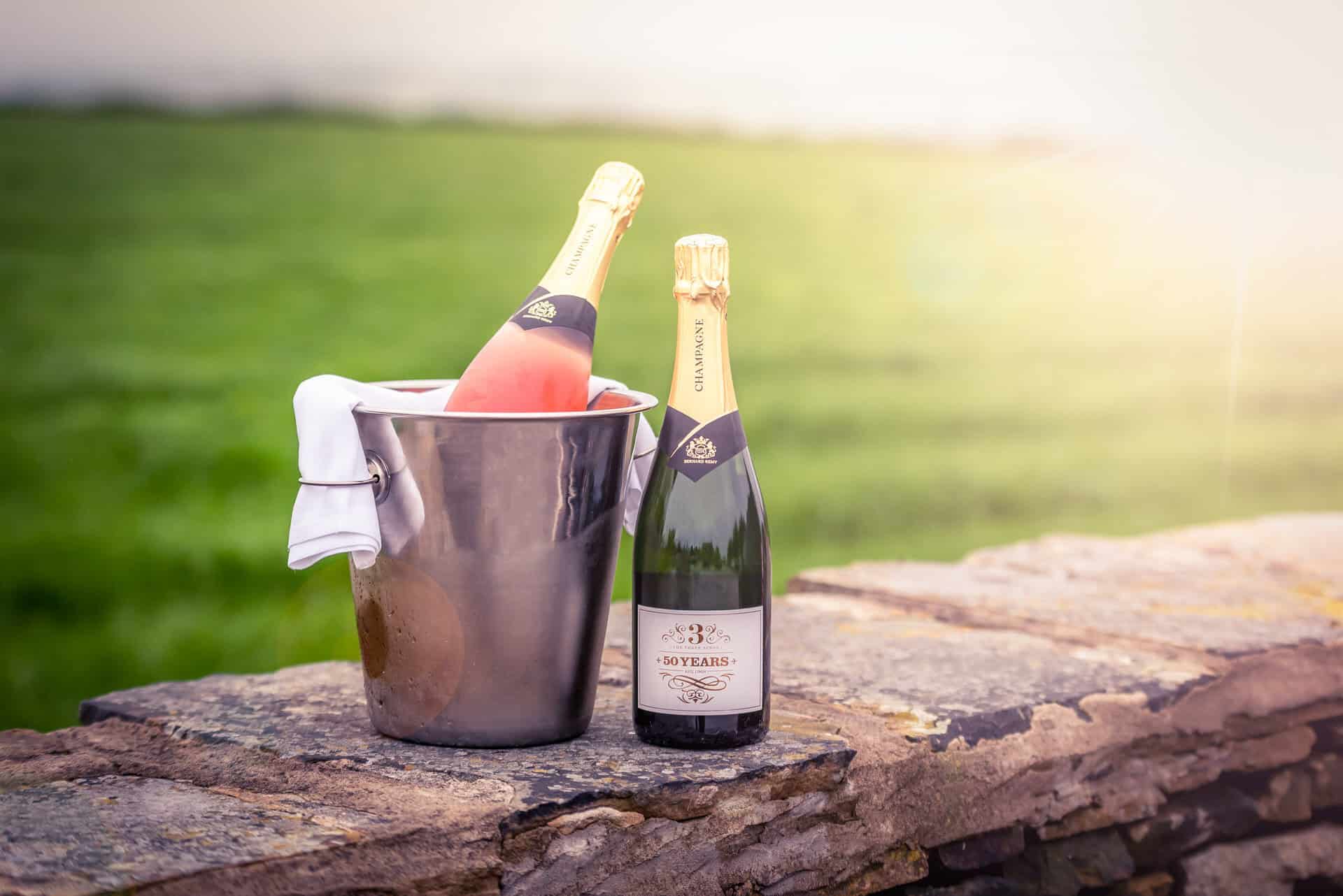 Two bottles of champagne sitting on a stone wall.