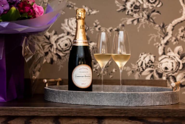 A bottle of champagne sits on a tray with flowers.