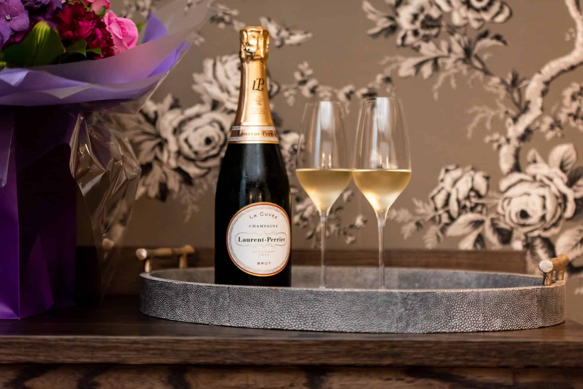 A bottle of champagne sits on a tray with flowers.