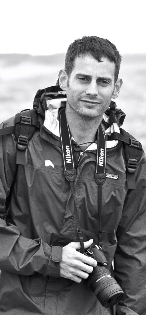 A black and white photo of a Dustin Smith holding a camera.