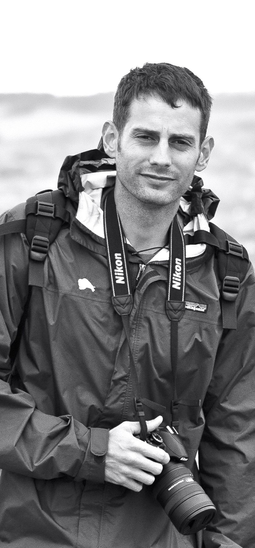 A black and white photo of a Dustin Smith holding a camera.